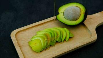 Top view of sliced and halved avocado on which honey is flowing on a black background video