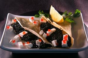 Pancake with black paddlefish caviar feta cheese cubes decorated with herbs and lemon photo