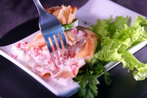 pancake with red caviar and mayonnaise made in a bag tied with green onions on a white square plate Parsley lettuce leaves Ukrainian Slavic food photo