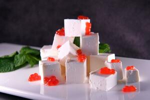 Feta cheese with red caviar decorated with herbs on a white plate. High quality photo