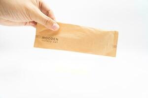 Hand holding Paper Packaging of Wooden Cutlery in Isolated, Eco Tableware, Disposable Cutlery, Recycle. Eco food packaging concept, zero waste paper, sustainability. photo