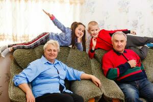 Happy young boy and girl with their laughing grandparents smiling at the camera as they pose together indoors photo