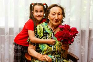 pequeño niña dando su genial abuela un rosado flor foto