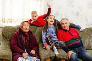 nietos saltando en sofá con su abuelos en el vivo habitación foto