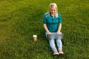 Top view of woman sitting in park on the green grass with laptop, hands on keyboard. Computer screen mockup. Student studying outdoors. Copy space for text photo