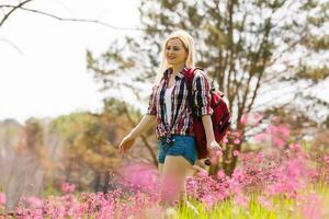 Happy adventurer female stands on the green mountain slope among flowering pink rhododendrons and looking into the distance. Epic travel in the mountains. Wide angle. photo