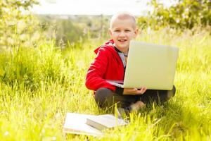 distancia aprendiendo. chico aprende al aire libre ordenador portátil. haciendo deberes en césped. el niño aprende en el Fresco aire. el niño manos y computadora foto