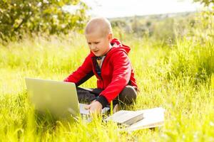 young boy with a books and laptop computer on green grass in the park photo