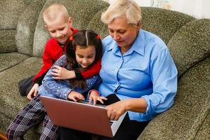 abuela con nietos utilizando ordenador portátil a hogar foto
