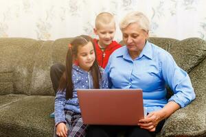 Grandmother with grandchildren using laptop at home photo