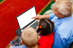 abuela con nietos utilizando ordenador portátil a hogar foto