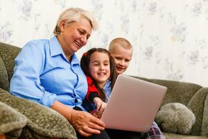 Grandmother with grandchildren using laptop at home photo