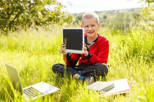 distancia aprendiendo. chico aprende al aire libre ordenador portátil. haciendo deberes en césped. el niño aprende en el Fresco aire. el niño manos y computadora foto