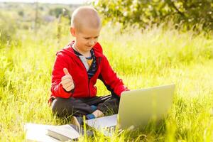 distancia aprendiendo. chico aprende al aire libre ordenador portátil. haciendo deberes en césped. el niño aprende en el Fresco aire. el niño manos y computadora foto