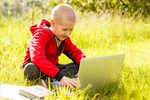 distancia aprendiendo. chico aprende al aire libre ordenador portátil. haciendo deberes en césped. el niño aprende en el Fresco aire. el niño manos y computadora foto