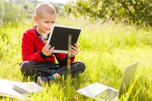 Distance learning. Boy learns autdoor laptop. Doing homework on grass. The child learns in the fresh air. The child's hands and computer photo