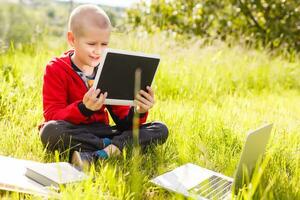 distancia aprendiendo. chico aprende al aire libre ordenador portátil. haciendo deberes en césped. el niño aprende en el Fresco aire. el niño manos y computadora foto