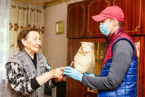 un mayor mujer corsé a hogar. comida entrega en un médico máscara a el anciano. foto