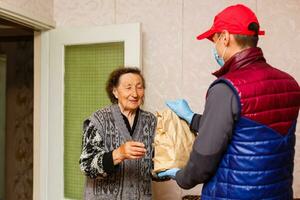 un mayor mujer corsé a hogar. comida entrega en un médico máscara a el anciano. foto