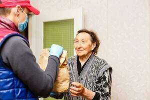 un mayor mujer corsé a hogar. comida entrega en un médico máscara a el anciano. foto