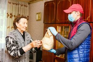 An elderly woman stays at home. Food delivery in a medical mask to the elderly. photo