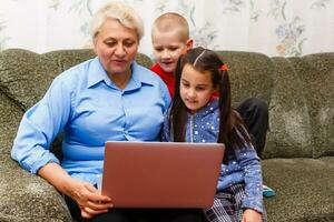 Grandmother with grandchildren using laptop at home photo