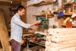 Satisfied cheerful joyful smiling woodmaster is standing near desktop in his workshop, workstation photo