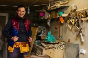 Satisfied cheerful joyful smiling woodmaster is standing near desktop in his workshop, workstation photo