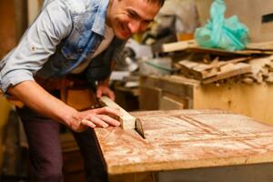 Satisfied cheerful joyful smiling woodmaster is standing near desktop in his workshop, workstation photo