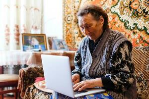 Old woman working on laptop computer at home, Grandma using notebook and searching on internet site photo