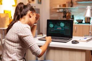 Angry hacker woman because of access denied while trying to attack government firewall. Programmer writing a dangerous malware for cyber attacks using performance laptop during midnight. photo