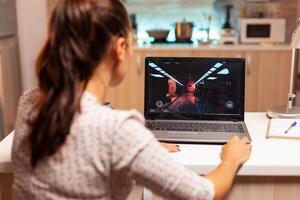 dama jugando juegos en ordenador portátil durante noche hora durante noche hora en hogar cocina. profesional jugador jugando en línea videop juegos en su personal computadora. friki ciber deporte foto