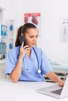 Medical receptionist talking with patient in hospital office and using laptop . Health care physician sitting at desk using computer in modern clinic looking at monitor. photo