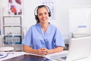 Young practitioner doctor working at the clinic reception desk talking with patients wearing headphones. Female nurse, doctor having a conversation with sick person during consultation, medicine. photo