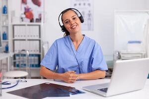 Young practitioner doctor working at the clinic reception desk talking with patients wearing headphones. Female nurse, doctor having a conversation with sick person during consultation, medicine. photo