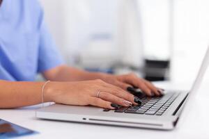 Close up of doctor hands typing on a laptop in a medical office. Health practitioner searching in hospital database using laptop in hospital cabinet, keyboard, job. photo