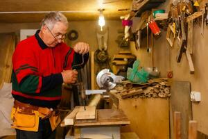 Satisfied cheerful joyful smiling woodmaster is standing near desktop in his workshop, workstation photo