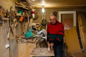 Satisfied cheerful joyful smiling woodmaster is standing near desktop in his workshop, workstation photo