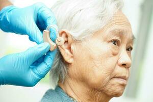 Doctor install hearing aid on senior patient ear to reduce hearing loss problem. photo