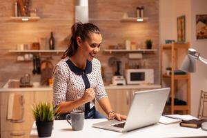 Portrait of happy businesswoman with clenched fist after finishing a deadline working from home. Employee using modern technology at midnight doing overtime for job, career, network, lifestyle. photo