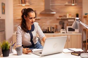 mujer utilizando crédito tarjeta en hogar cocina a hacer en línea pago. creativo dama haciendo en línea transacción utilizando digital cuaderno conectado a Internet. foto