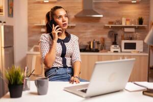 Concentrated businesswoman during phone call late at night from home office. Employee using modern technology at midnight doing overtime for job, business, busy, career, network, lifestyle ,wireless. photo