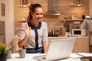 mujer sonriente y diciendo Hola durante vídeo conferencia mientras trabajando desde hogar. empleado utilizando moderno tecnología a medianoche haciendo tiempo extraordinario para trabajo, negocio, carrera profesional, red, estilo de vida ,inalámbrico. foto