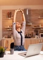 Exhausted freelancer woman streching while working on a deadline late at night. Employee using modern technology at midnight doing overtime for job, business, busy, career, network, lifestyle ,wireless. photo