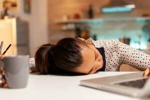 Woman falling asleep with head on the table while working from home on a deadline. Employee using modern technology at midnight doing overtime for job, business, career, network, lifestyle ,wireless. photo