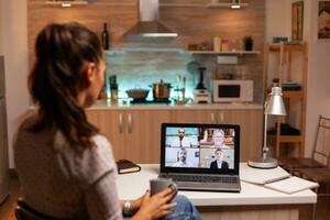 mujer de negocios teniendo un vídeo conferencia con equipo durante medianoche utilizando ordenador portátil en hogar cocina. corporativo reunión utilizando moderno tecnología, ordenador portátil tarde a noche , tecnología, agencia, tutor, trabajar, discusión. foto