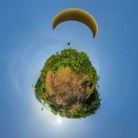 green grass little planet in blue sky with yellow paragliding parachute photo