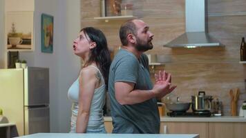 Couple with trust issues fighting back to back. Furious, irritated, frustrated, jealous unhappy couple screaming accusing to each other having family conflict disputing sitting in the kitchen. photo