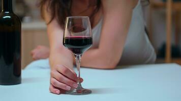 Close up of woman holding a glass of red wine on the table. Unhappy person suffering of migraine, depression, disease and anxiety feeling exhausted with dizziness symptoms having alcoholism problems. photo