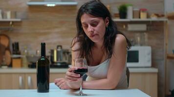 Thoughtful wife looking at a glass of wine sitting on the chair. Unhappy person suffering of migraine, depression, disease and anxiety feeling exhausted with dizziness symptoms having alcoholism problems. photo